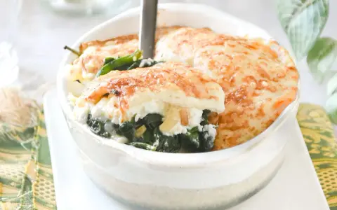 Deliciosa lasaña de espinacas gratinada, servida en un cuenco blanco. El queso dorado y burbujeante cubre las capas de espinacas y ricotta.