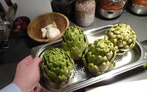 Quatre artichauts verts prêts pour la cuisson vapeur. Une main tient le plateau.