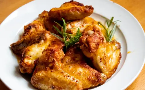 En tallrik med gyllene, saftiga kycklingvingar, garnerade med rosmarin. Perfekt för en hållbar måltid.