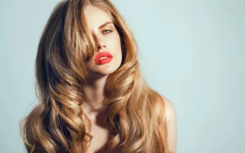 Kobieta z burzą falujących, blond włosów w stylu wolf cut, z wyrazistą czerwoną szminką.