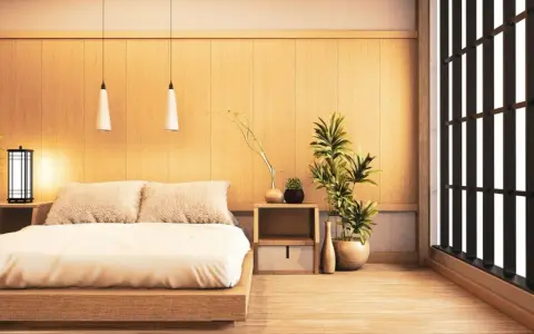 Une chambre style japonais épurée avec un lit bas en bois, des coussins douillets, des plantes vertes et une fenêtre aux persiennes sombres.