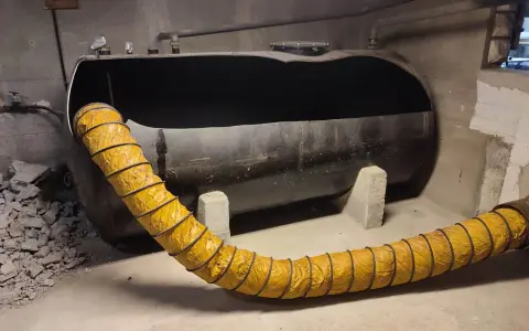 Gros réservoir de fioul noir, vide, avec un tuyau jaune flexible. Projet ma prime rénov cuve fioul en cours.