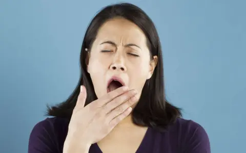 Une femme bâille, la main devant la bouche. Elle semble avoir besoin d'une pause pour réviser la conjugaison.