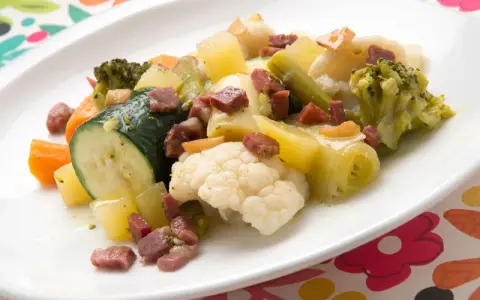 Un colorido panache de verduras con brócoli, coliflor, calabacín, zanahoria y patatas, salpicado de trocitos de jamón.