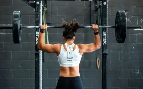 Femme musclée soulevant une barre chargée, prête pour un superset musculation intense.