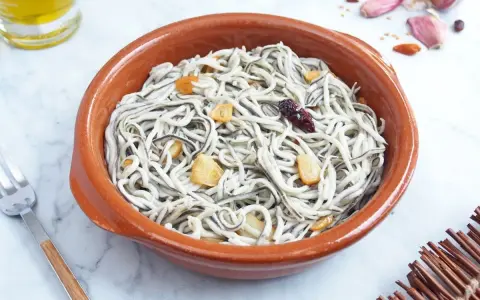 Un cuenco de barro con gulas al ajillo, adornado con láminas de ajo dorado y un chile seco.