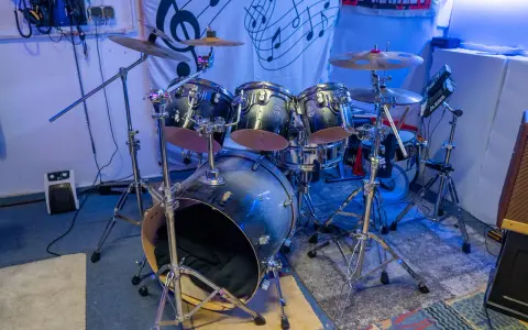 Der **Aufbau Schlagzeug** ist bereit für den nächsten Gig. Glänzende Trommeln und Becken stehen auf stabilen Stativen, beleuchtet von blauem Licht.