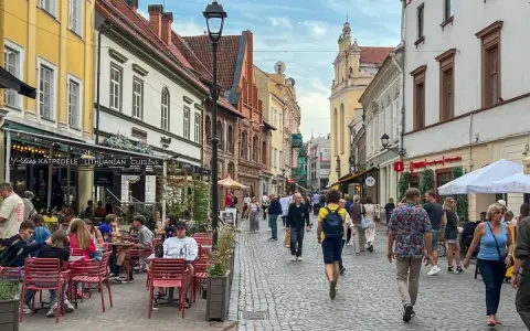 Tłum ludzi spaceruje brukowaną ulicą w Wilnie, siedząc przy stolikach restauracyjnych. Czy wyjazd na Litwę jest bezpieczny? Wygląda na to, że tak!