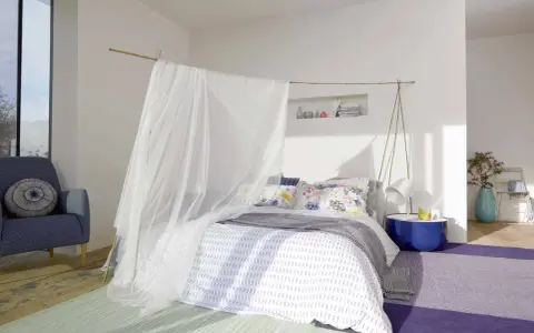 Acogedora habitación marinera con cama con dosel de tul, sillón azul y alfombras de colores.