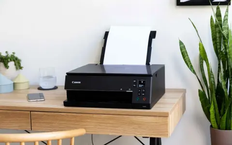 Schwarzer Canon Pixma Drucker mit WLAN verbinden. Ein Smartphone und ein Glas Wasser stehen daneben.