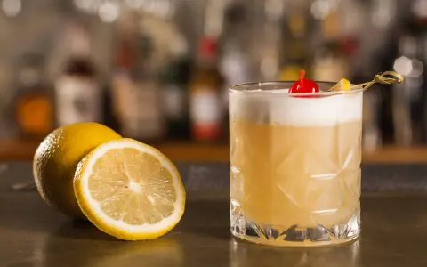Orzeźwiający drink z amaretto, ozdobiony wiśnią i cytryną, stoi obok świeżych cytryn na barze.