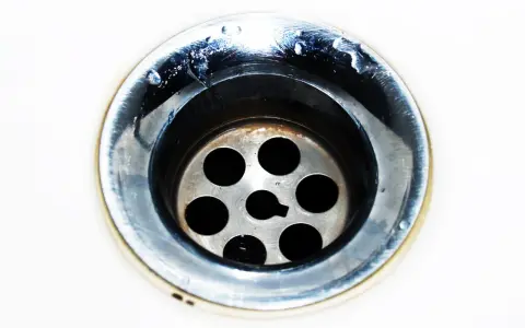 Gouttes d'eau stagnent dans un évier bouché mais pas de bouchon visible. Le métal du siphon est sale et usé.