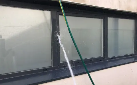 Agua salpicando sobre un perfil de aluminio de ventana, creando condensación y gotas.