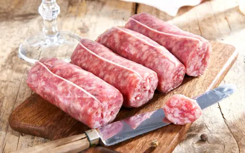 Frische Salsiccia zum Zubereiten liegen auf einem Holzbrett. Ein Messer mit einer Scheibe daneben deutet auf die Vorbereitung hin.