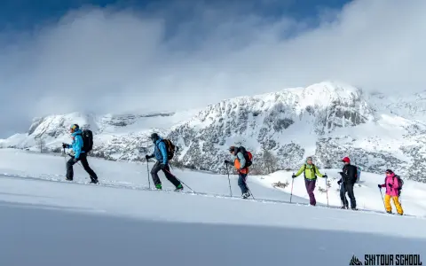 Grupa ludzi na skitouringu wspina się po ośnieżonych zboczach gór. To właśnie skitouring co to za aktywność!