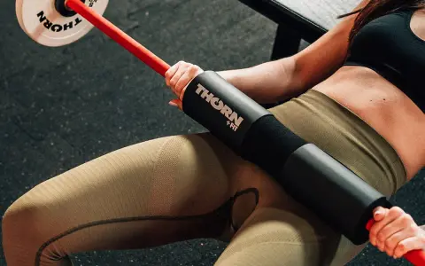 Kobieta wykonuje hip thrust w domu z gryfem i obciążeniem.