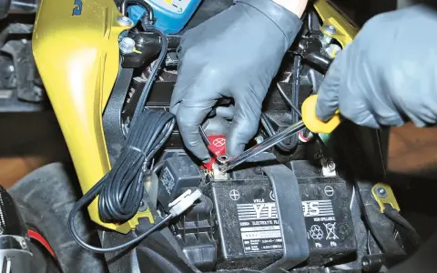 Mani guantate usano una chiave per staccare la batteria moto, scollegando il cavo rosso.