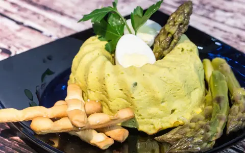 Delizioso flan di asparagi, guarnito con uovo sodo, asparagi freschi e grissini croccanti su un piatto nero.