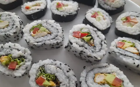 Pyszne domowe sushi z kurczakiem, awokado i warzywami, posypane czarnym sezamem.