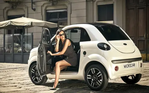 Elegancka kobieta w okularach przeciwsłonecznych wysiada z białego samochodu Microcar, idealnego na miejskie wypady bez prawa jazdy.