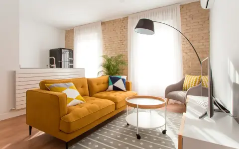 Sofá mostaza con cojines geométricos, mesa auxiliar redonda y alfombra gris. Los colores que combinan con el mostaza resaltan en esta sala.