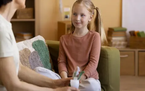 Rozmowa psychologa z rodzicem o zdrowiu dziecka. Dziewczynka z piegami słucha uważnie.