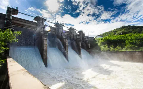 Ein Damm mit mehreren offenen Schleusen, aus denen kräftig Wasser strömt. Ein Beispiel für erneuerbare Energien durch Wasserkraft.