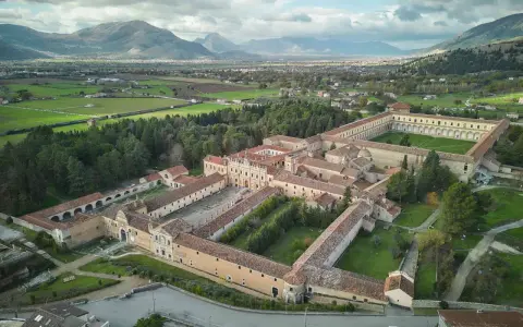 Vasta Certosa di Padula, un complesso monastico imponente con cortili verdi, circondato da alberi e montagne sullo sfondo.