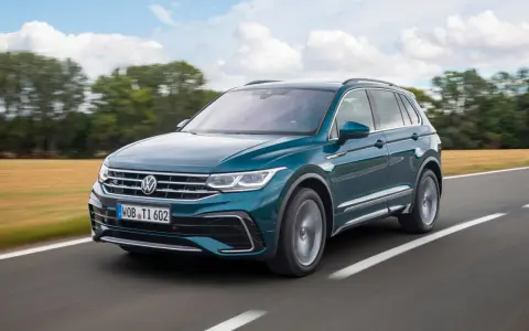 Un Volkswagen Tiguan R-Line verde oscuro se desplaza por una carretera rural, con campos dorados y árboles borrosos al fondo.