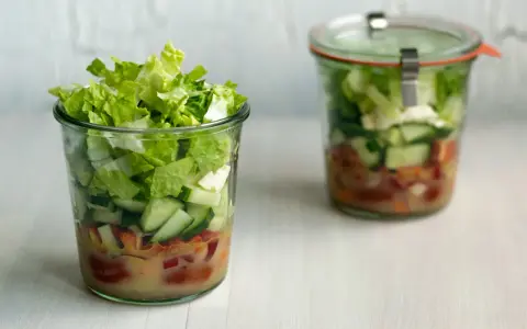 Frischer Salat im Glas, perfekt für eine Party. Schichten aus knackigem Salat, Gurken und Tomaten mit Dressing.