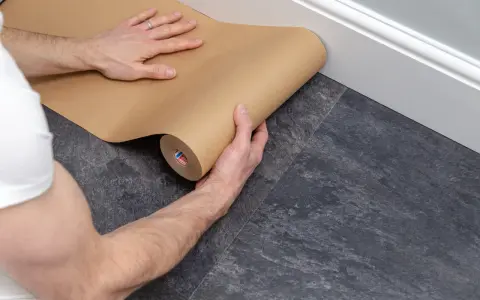 Ręce rozwijają brązowy papier, zabezpieczając podłogę podczas remontu.