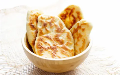 Kilka świeżo upieczonych chlebków naan w drewnianej misce.