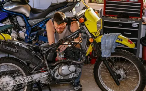 Mężczyzna majstruje przy żółtym motocyklu Suzuki. Rozrusznik kręci, a motocykl nie odpala.