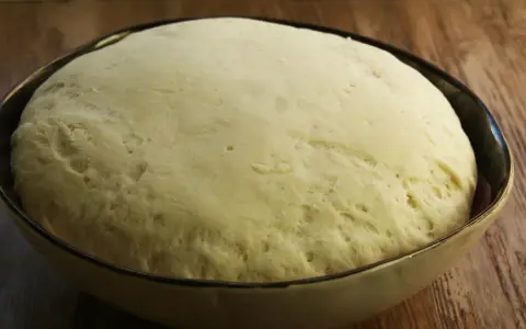 Wyrośnięte ciasto drożdżowe w misce, gotowe do pieczenia pizzy.