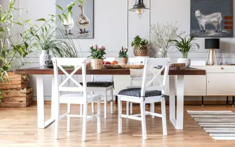 Comedor con mesa de madera oscura y sillas blancas, un ejemplo perfecto de cómo combinar muebles blancos y madera oscura. Plantas y cuadros decoran el espacio.