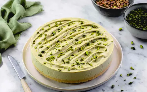 Cheesecake al pistacchio cremosa, decorata con granella verde brillante. Un dolce invitante pronto per essere gustato.