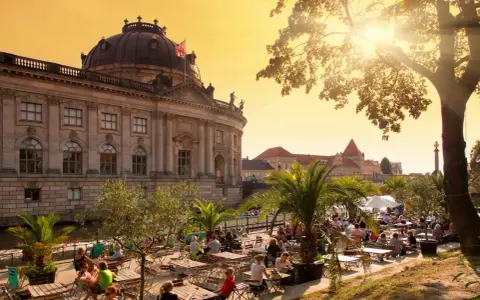 En solig eftermiddag vid en uteservering i Berlin, med en imponerande byggnad i bakgrunden. Kanske en paus innan nattåg Berlin.