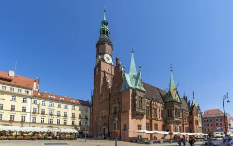Rynek we Wrocławiu z Ratuszem, gdzie mieści się muzeum sztuki mieszczańskiej. Wokół kawiarnie i ludzie spacerujący.