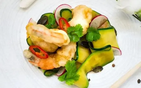 Chrupiące tempura do krewetek z cukinią, rzodkiewką i chili na białym talerzu.