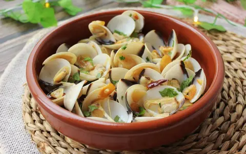 Deliciosas almejas al ajillo, servidas en una cazuela de barro, con ajo laminado y perejil fresco.