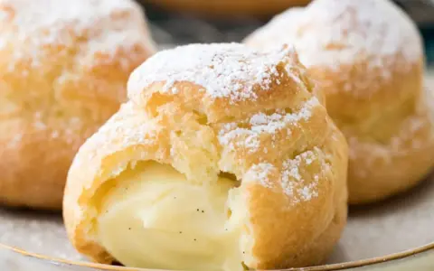 Trois choux à la crème généreusement garnis de crème pâtissière à la vanille, saupoudrés de sucre glace.