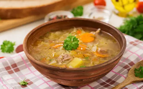Najprostszy kapuśniak w glinianej misce, z kawałkami mięsa, ziemniaków i marchewki, ozdobiony natką pietruszki.