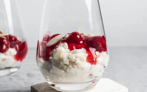 Delicioso arroz con leche asturiano cremoso, coronado con cerezas rojas y almendras laminadas en un vaso.