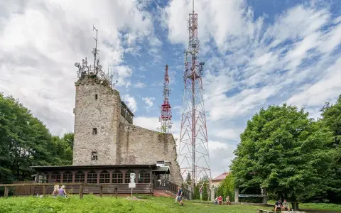 Kamienna wieża widokowa na Chełmcu, obok niej wysokie maszty telekomunikacyjne. Ludzie odpoczywają na trawie.