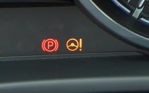 Kontrolka PS Nissan: czerwony symbol hamulca ręcznego i pomarańczowa kontrolka układu kierowniczego z wykrzyknikiem.