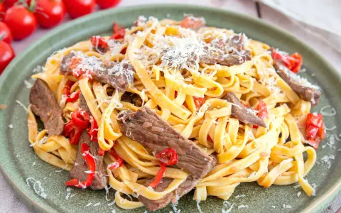 Pasta mit Rinderfiletstreifen, Tomaten und Parmesan auf einem grünen Teller.