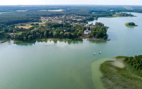 Malownicze jezioro Niesłysz z widokiem na wieś, lasy i dwa żaglówki na wodzie.