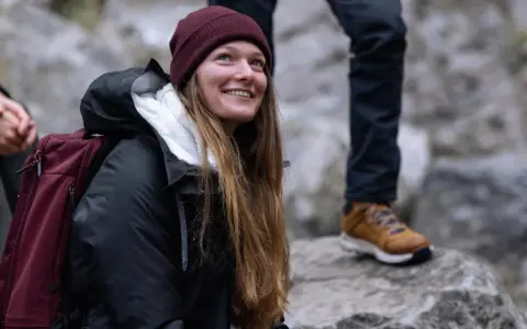 Uśmiechnięta kobieta w bordowej czapce i czarnej kurtce z bordowym plecakiem.