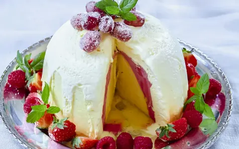 En imponerande dessert till nyår: en kupolformad glassbakelse med lager av gul och rosa glass, dekorerad med färska bär och mynta.