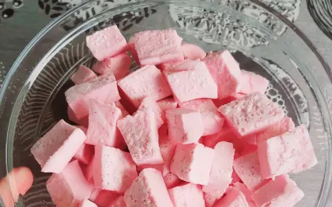 Nubes de golosina rosas cortadas en cubos en un bol de cristal, perfectas para recetas dulces.